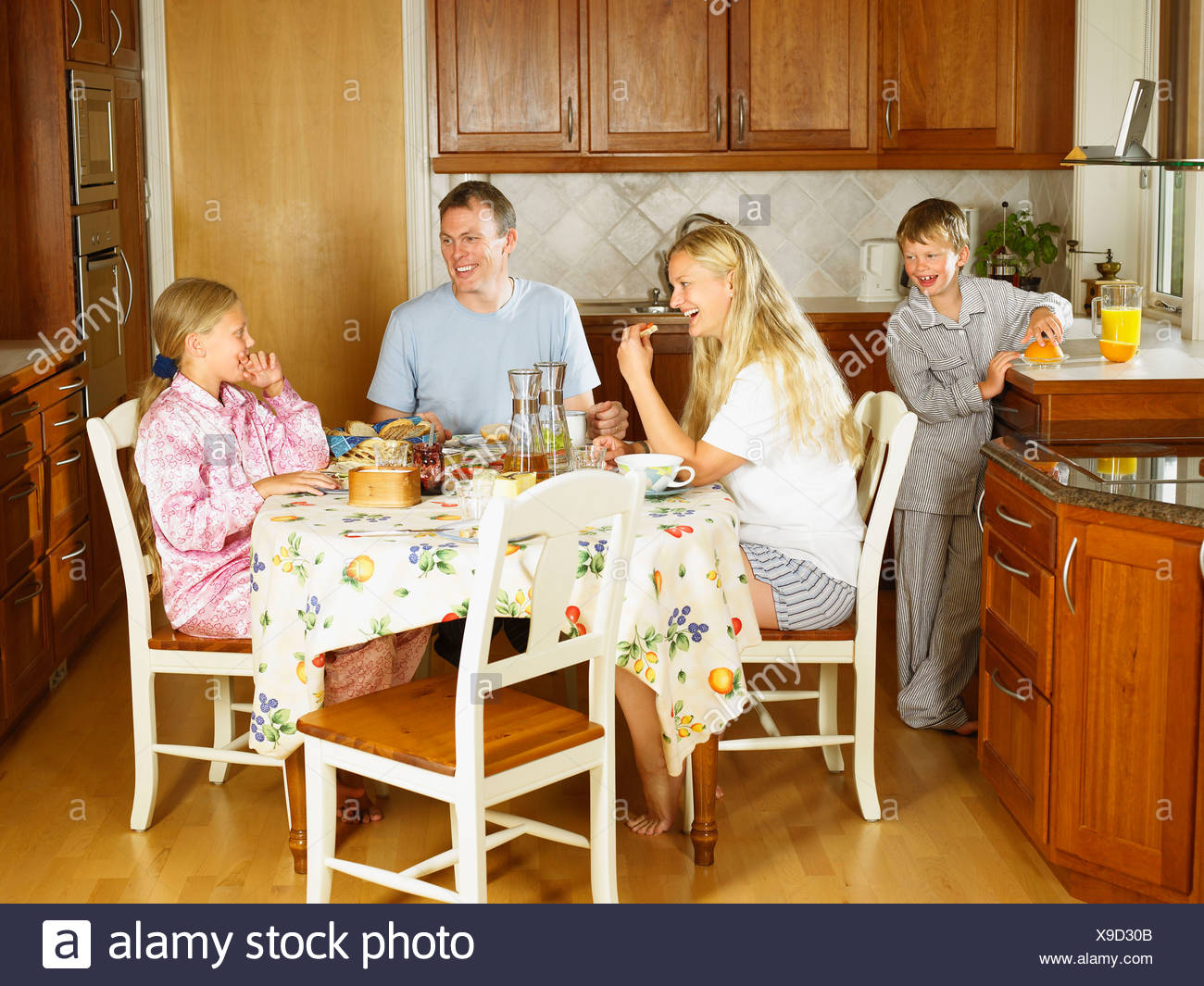Family Sitting At Kitchen Table Eating Breakfast Smiling Stock