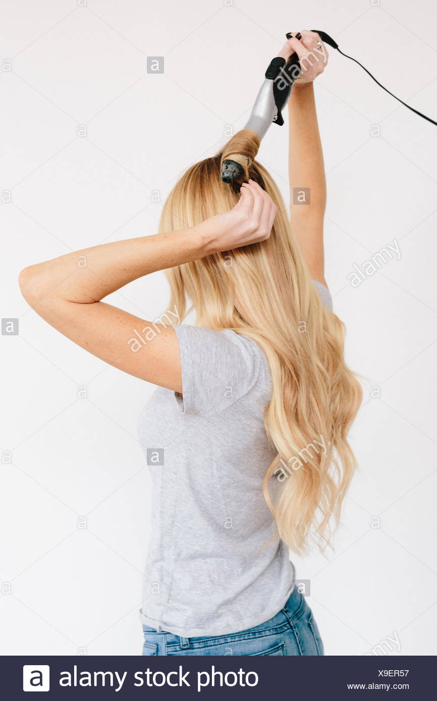 A Young Woman With Long Blond Wavy Hair Using Curling Tongs Side