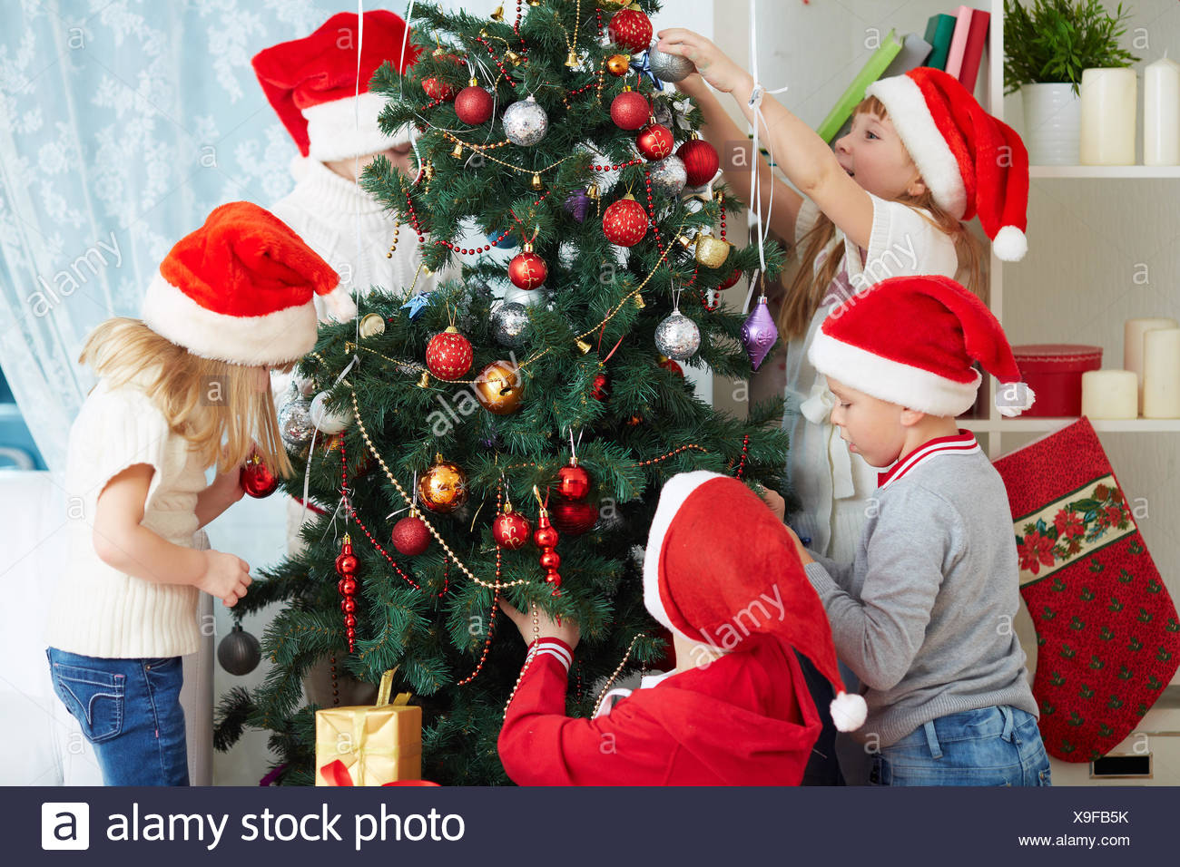 Group Of Adorable Kids In Santa Caps Decorating Xmas Tree Stock