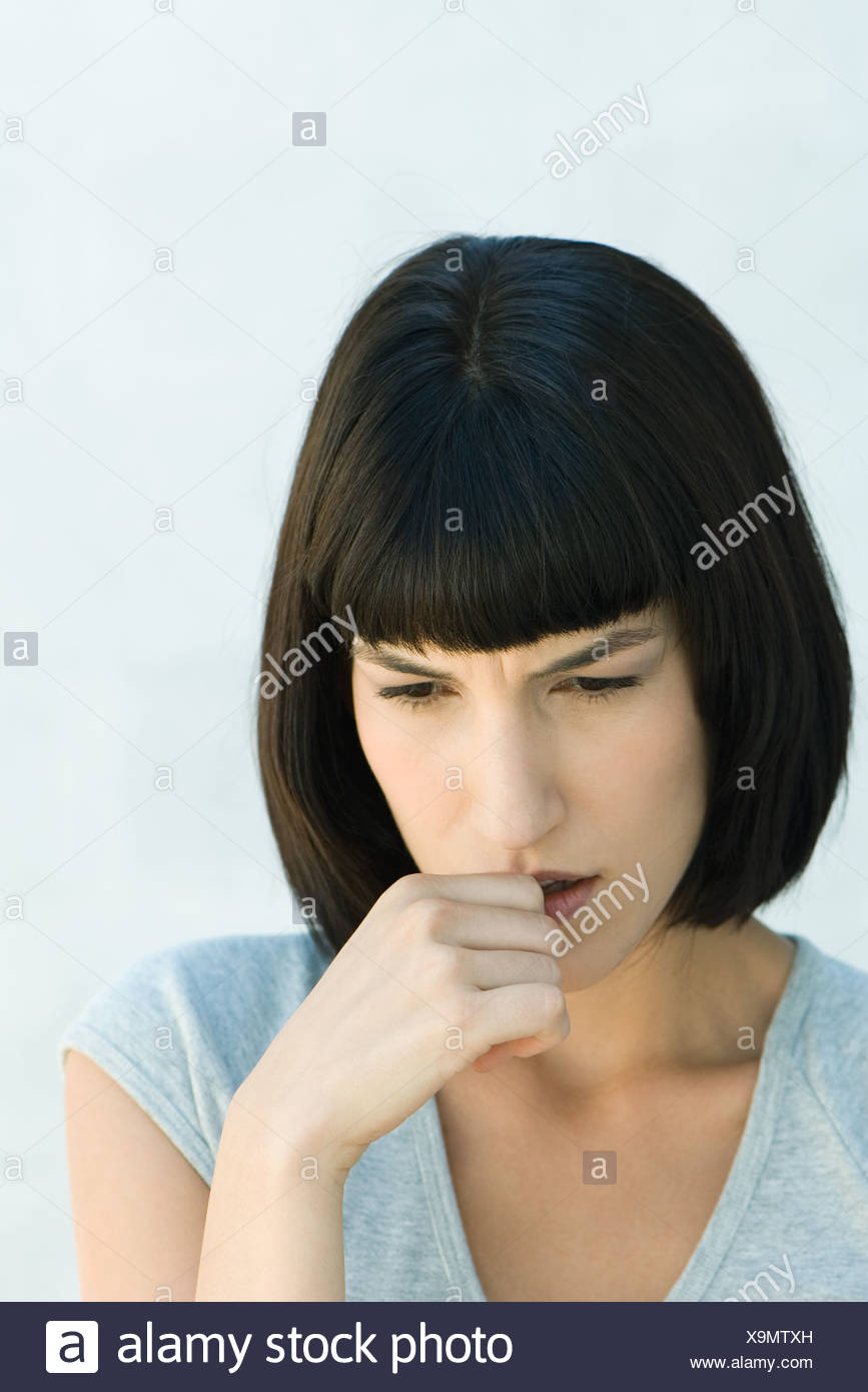 Woman biting thumb and looking down, head and shoulders, portrait Stock Photo