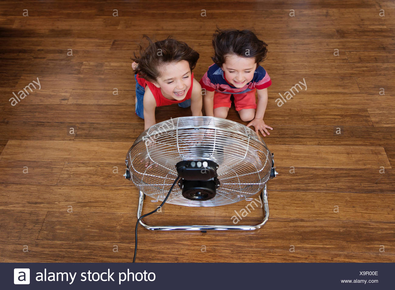Twin Brothers Kneeling On Wooden Floor In Front Of Fan Having Fun