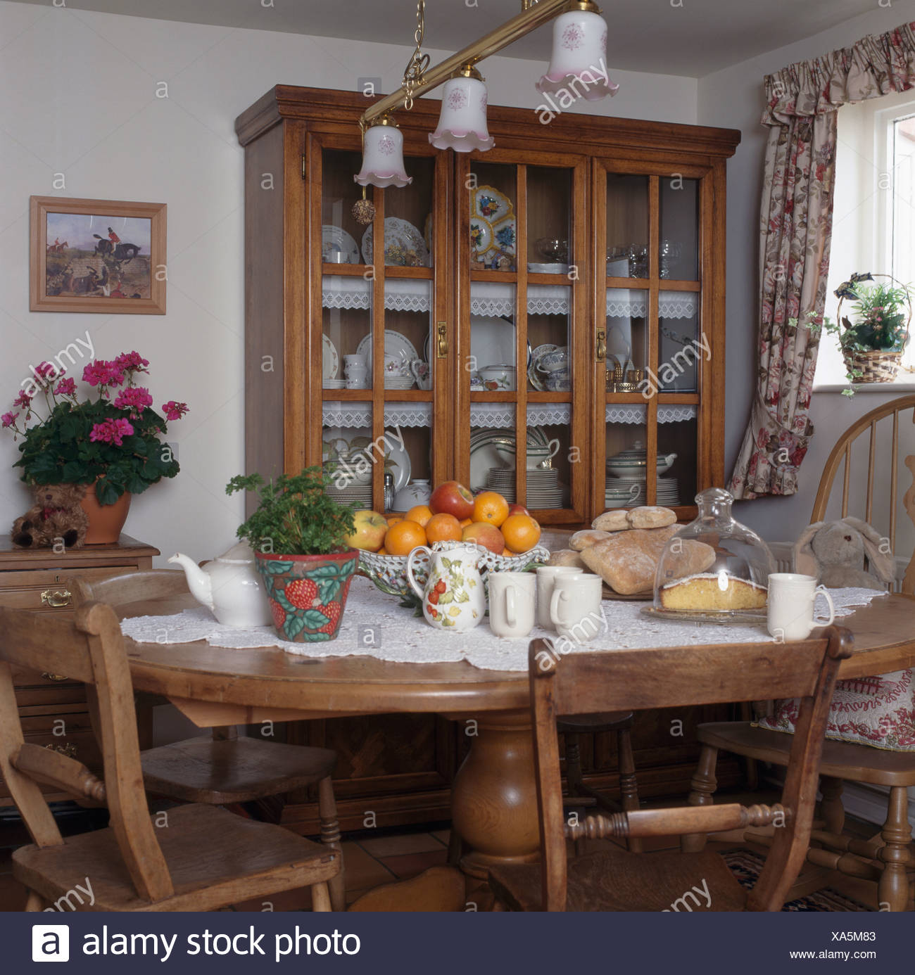 Glass Fronted Dresser In Cottage Dining Room With Bowl Of Oranges And White Cupboards On Circular Pine Table With Lace Cloth Stock Photo Alamy