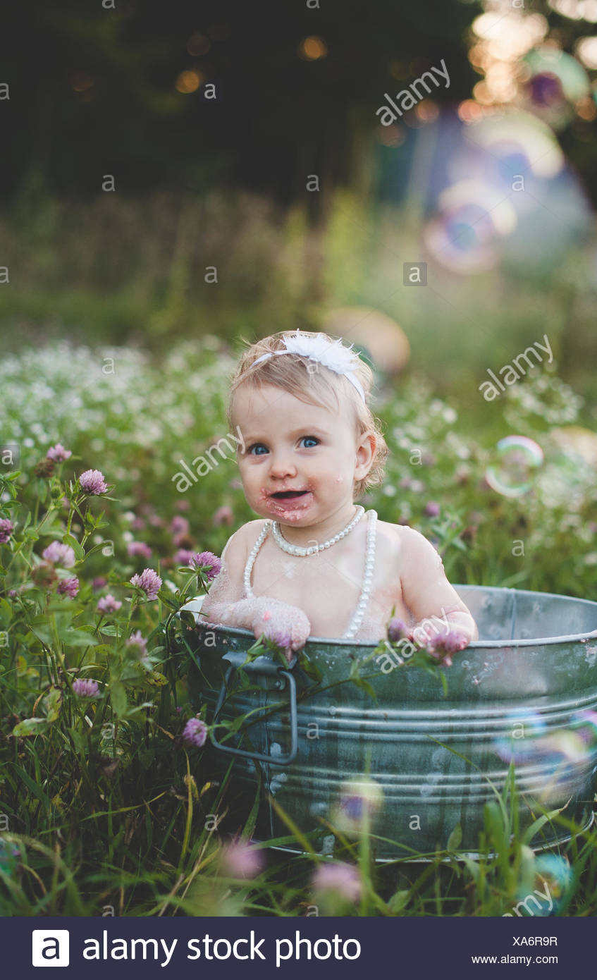 Portrait of baby girl bathing in a tin bathtub in a wild flower meadow Stock Photo