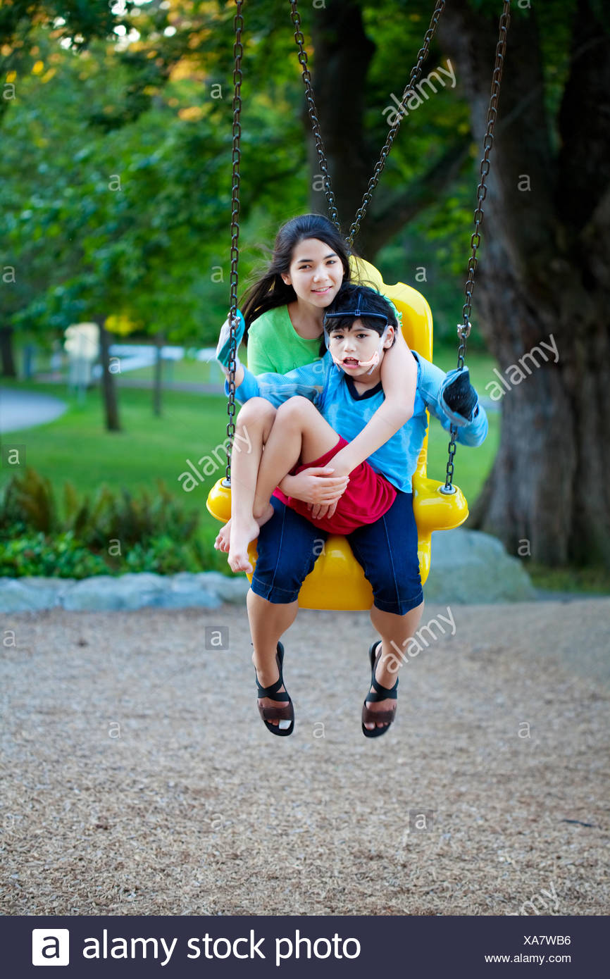 Big Sister Holding Disabled Brother On Special Needs Swing