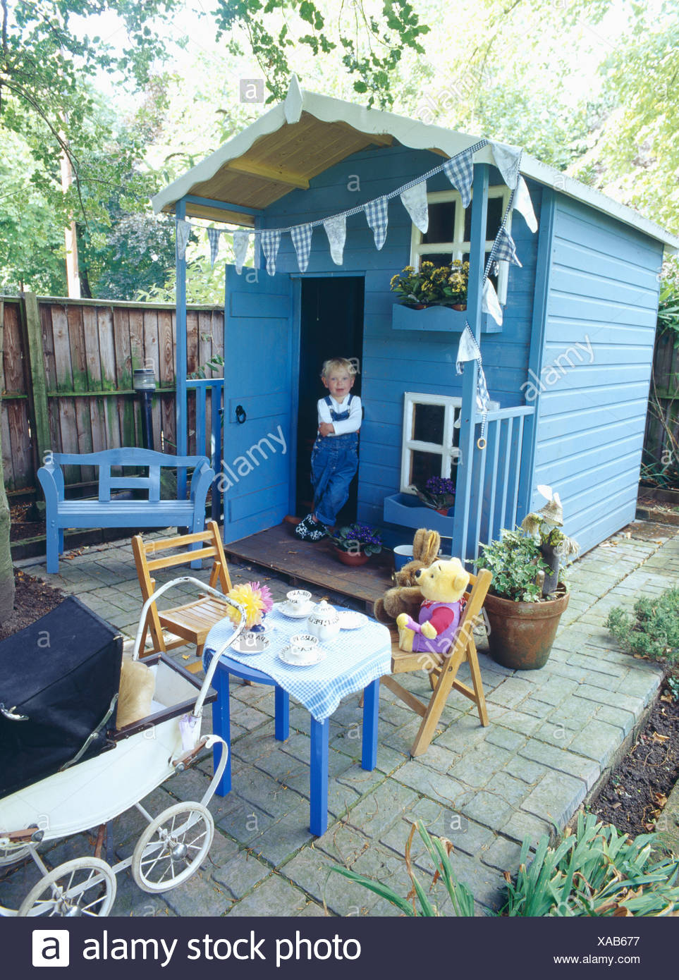 Small Girl Wearing Dungarees Standing In Doorway Of Blue Wooden