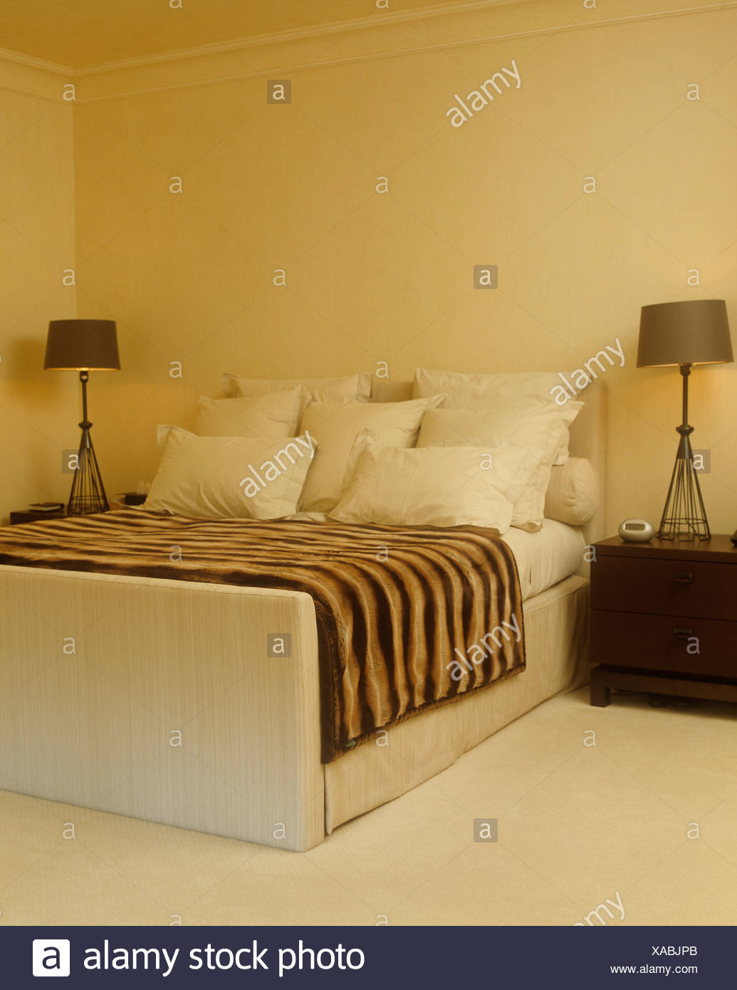 Faux Animal Skin Throw On Suede Upholstered Bed Piled With Pillows