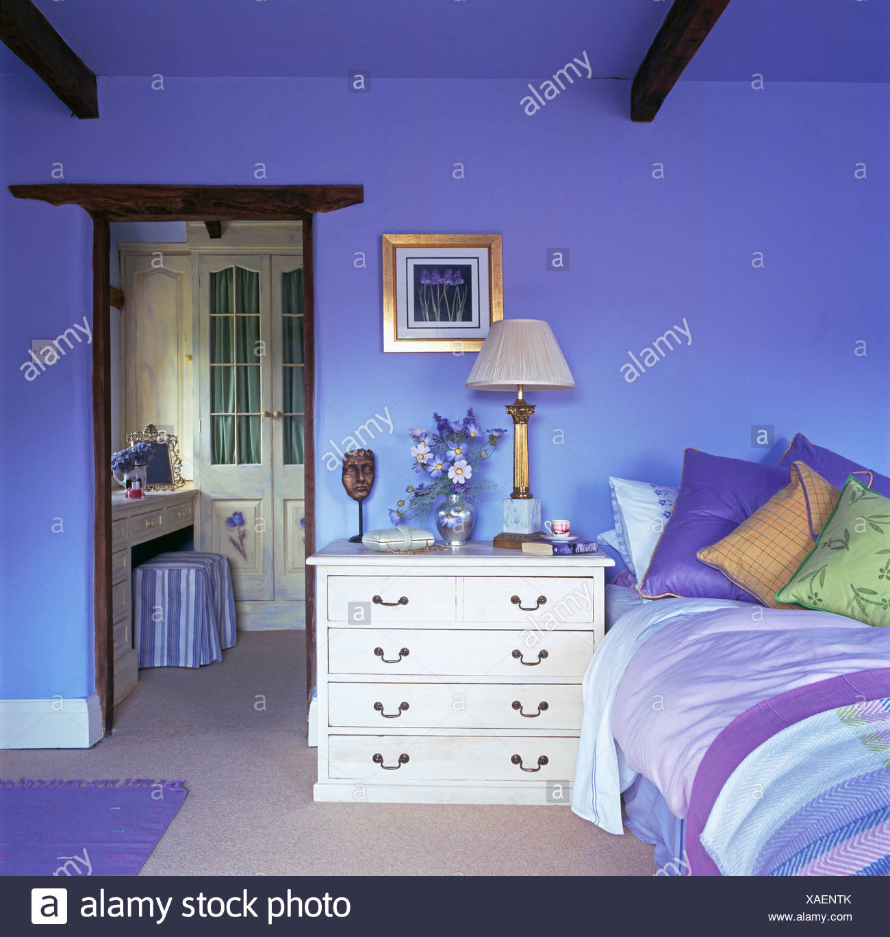White Chest Of Drawers Beside Bed Piled With Colorful Cushions In