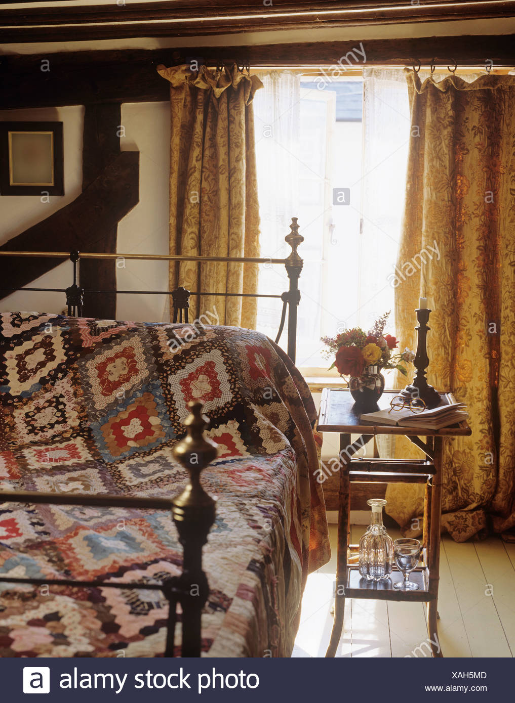Small Bamboo Table Beside Brass Bed With Patchwork Quilt In