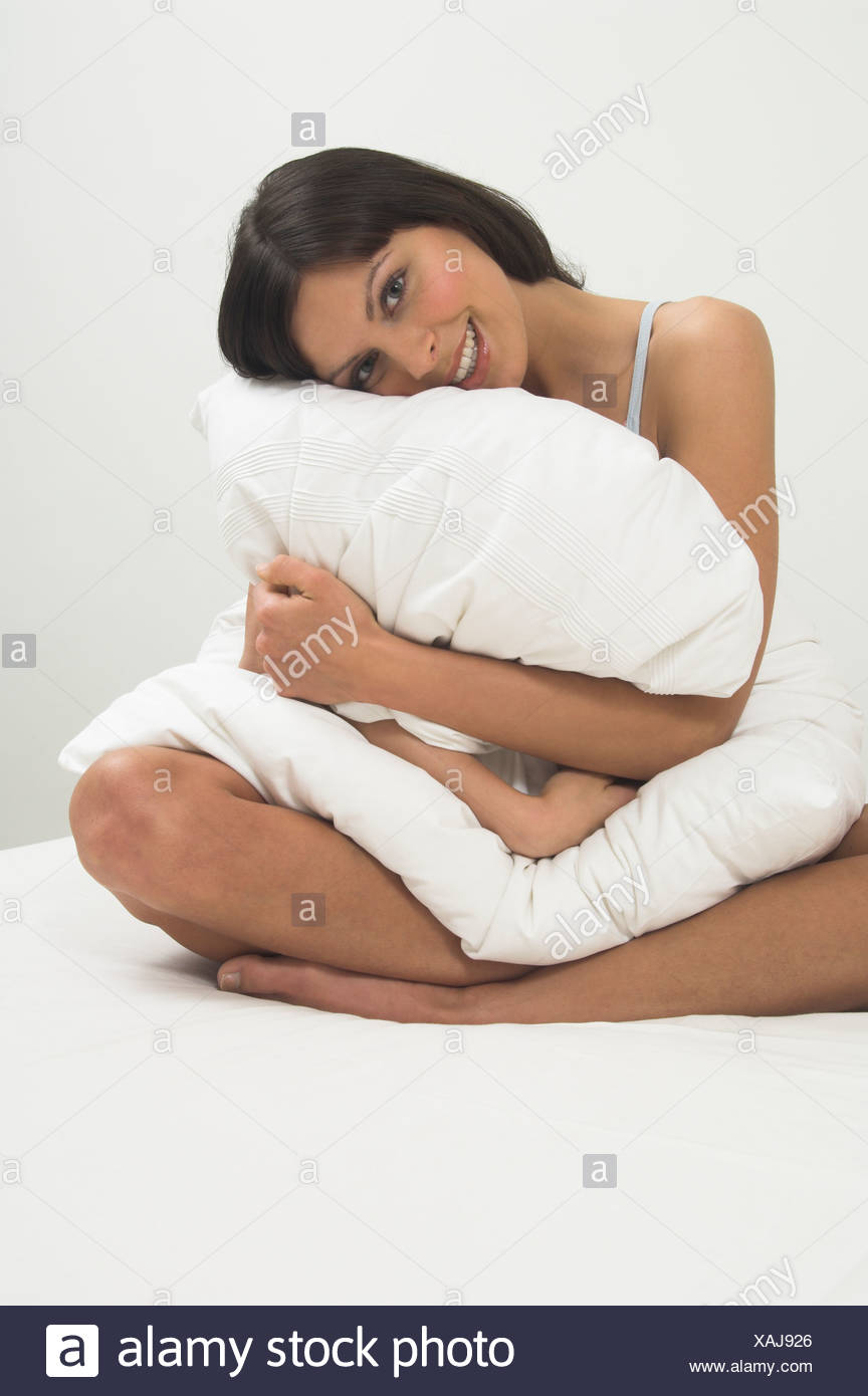 Portrait Of Young Woman Sitting On Bed And Cuddling Pillow Stock