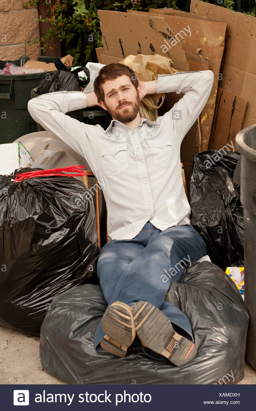 Man sitting on pile of bin bags Stock Photo