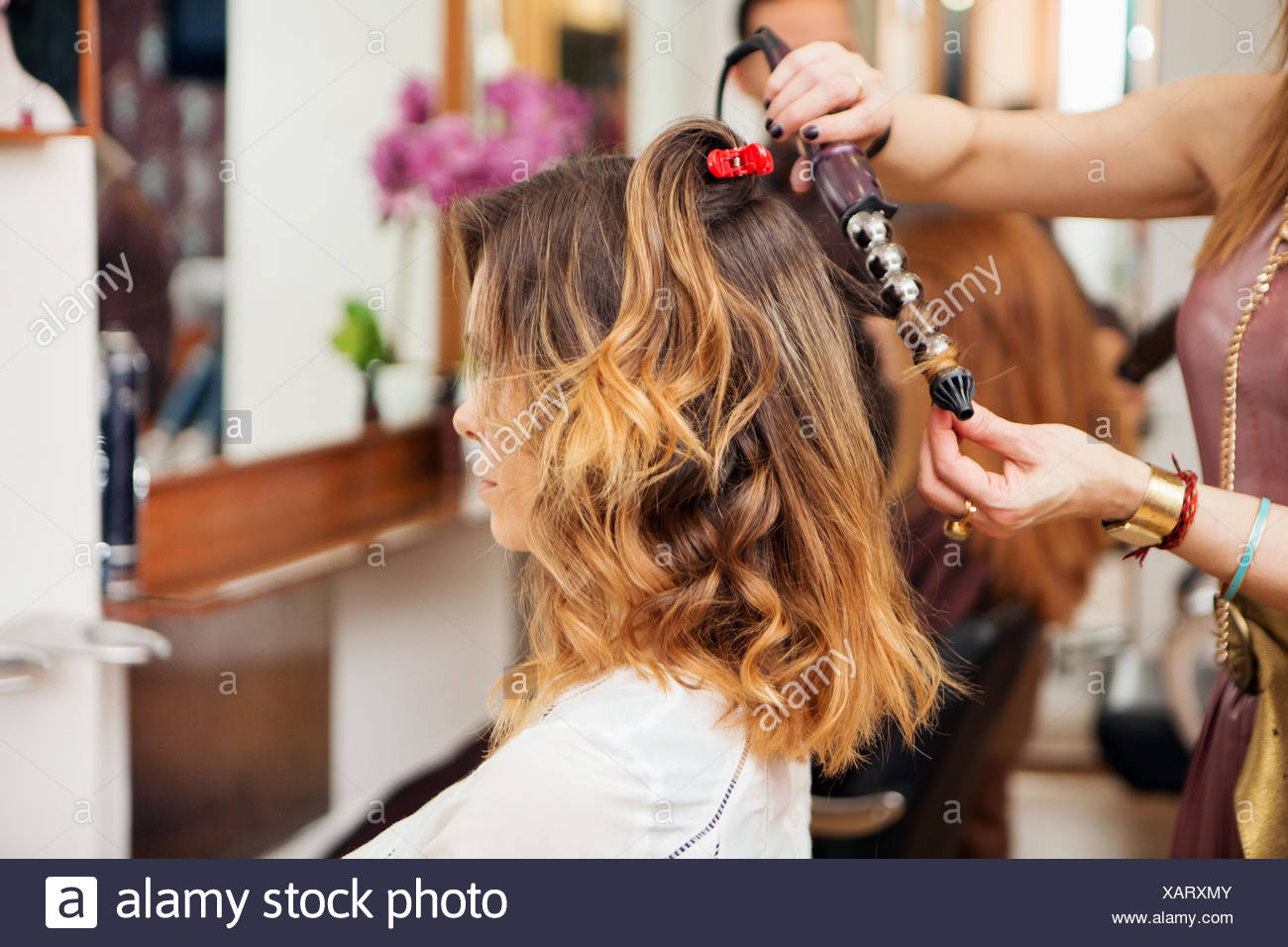 Hairdresser Using Curling Tongs On Customer S Long Brown Hair In