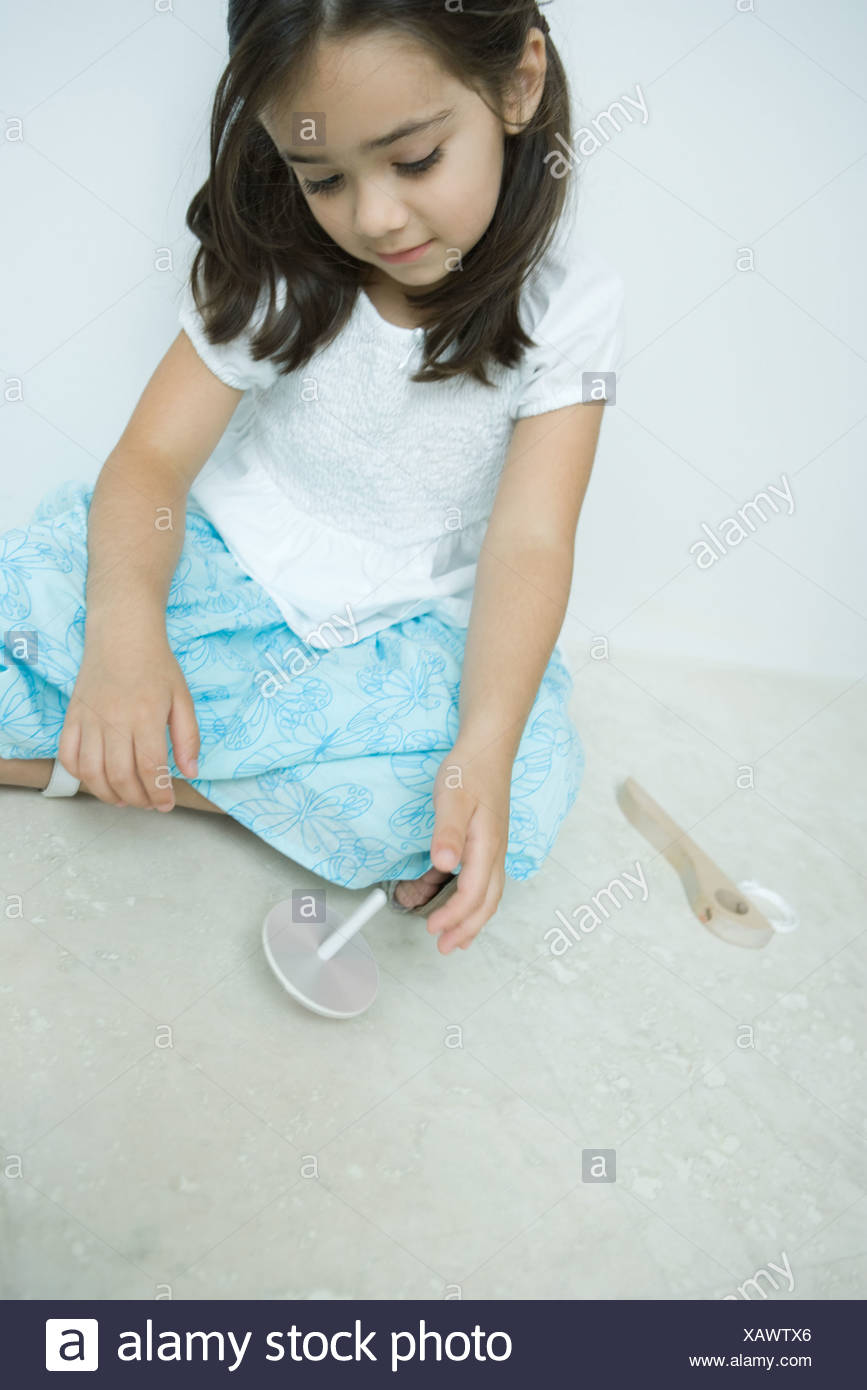 Girl sitting on the ground playing with top, close-up Stock Photo