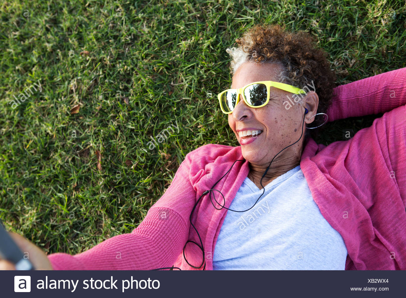Portrait of senior woman lying on grass wearing sunglasses Stock Photo