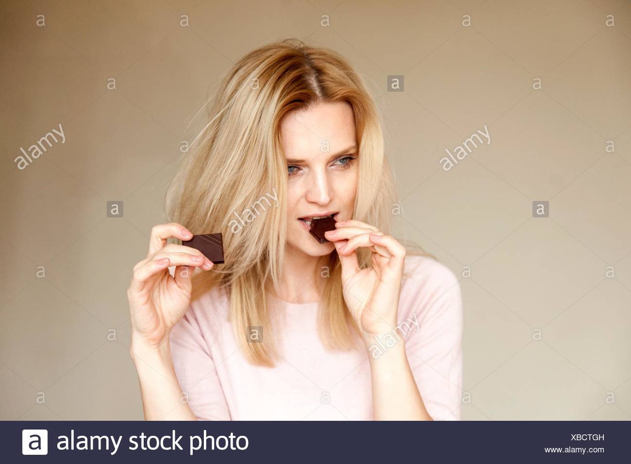 Portrait of beautiful woman with long blond hair eating chocolate bar Stock Photo