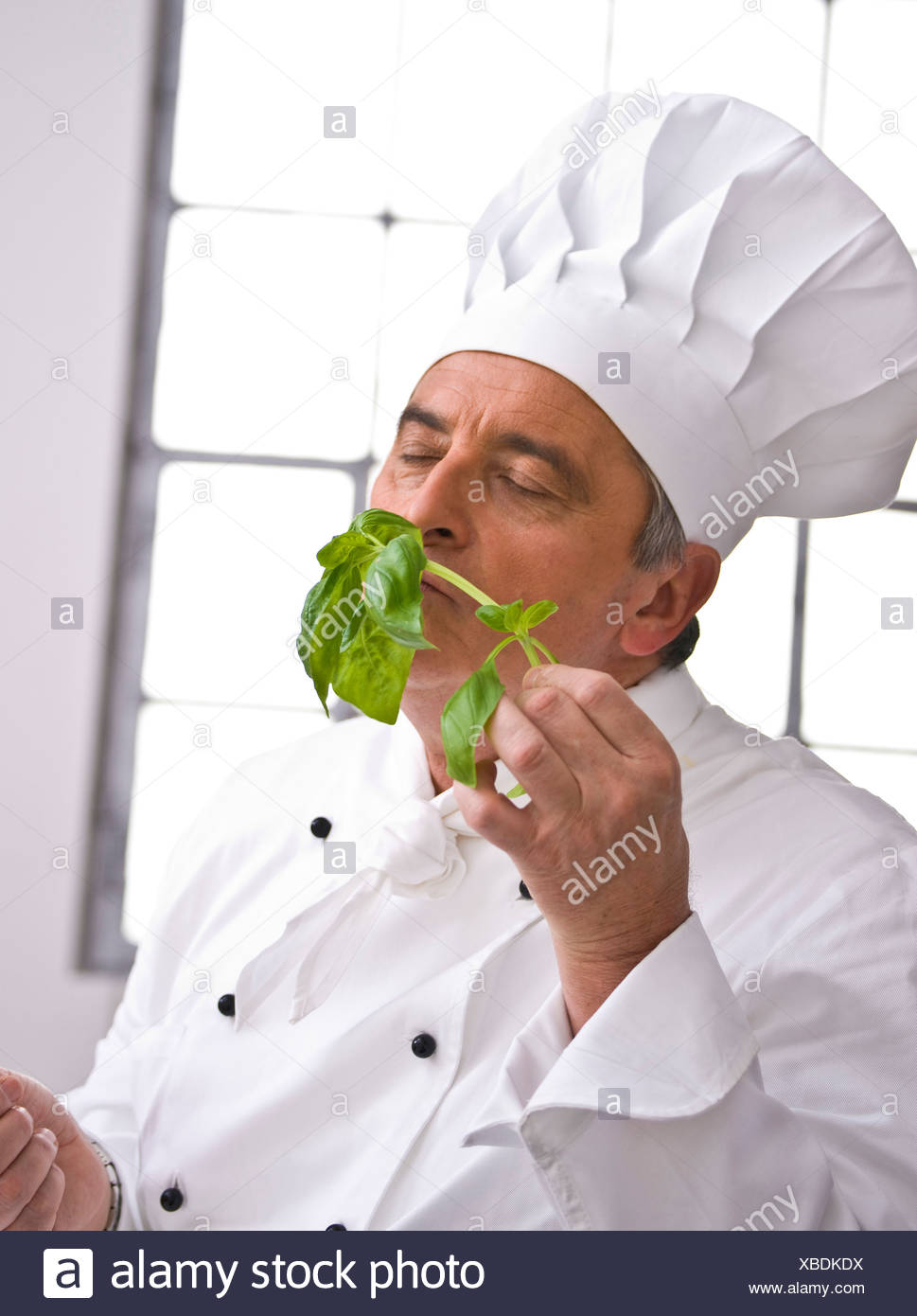 Chef Wearing A Chef S Hat Smelling A Sprig Of Basil Stock Photo Alamy