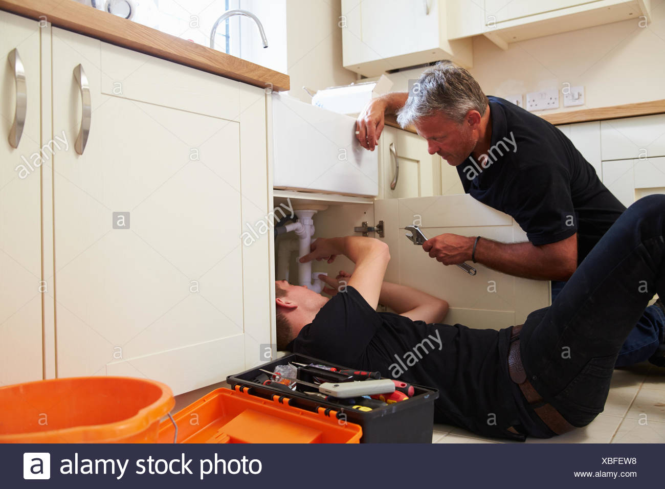 Plumber Teaching A Young Apprentice To Fix A Kitchen Sink