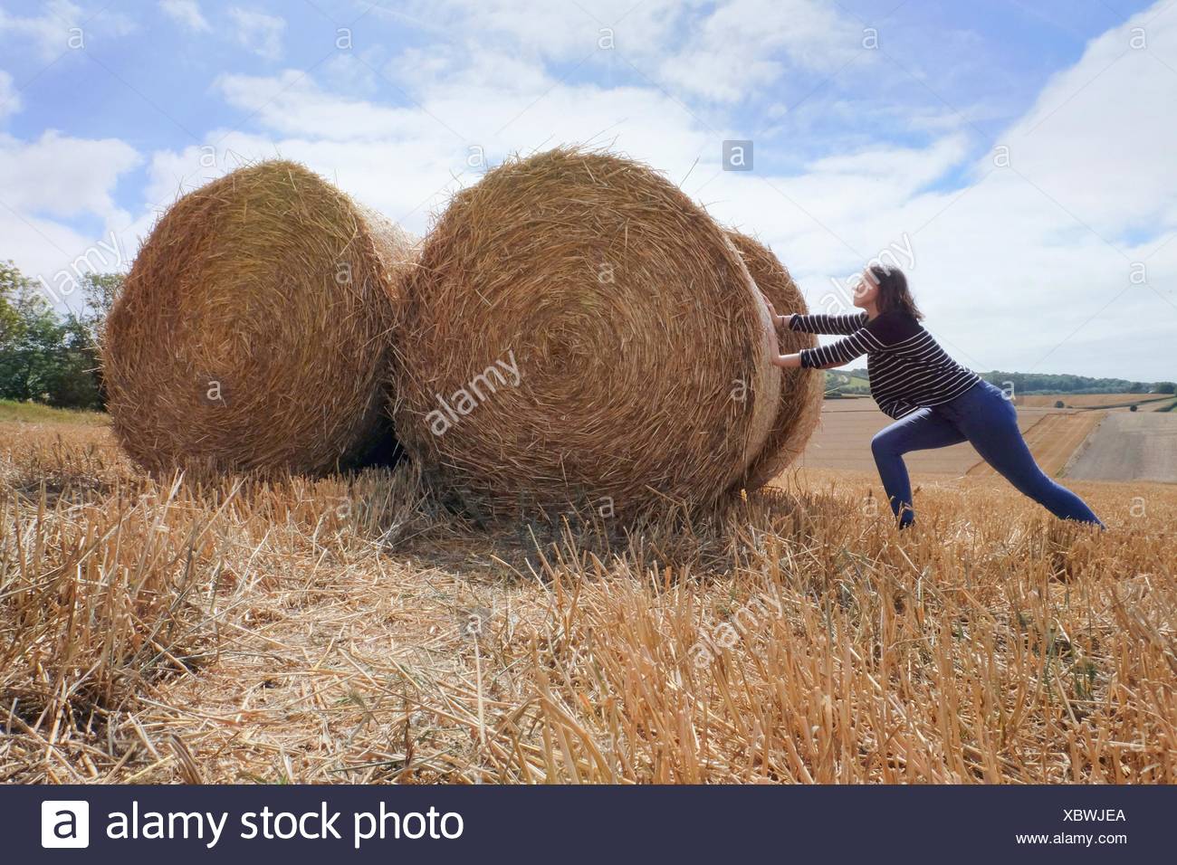 Young woman pretending to push haystacks in harvested field Stock Photo