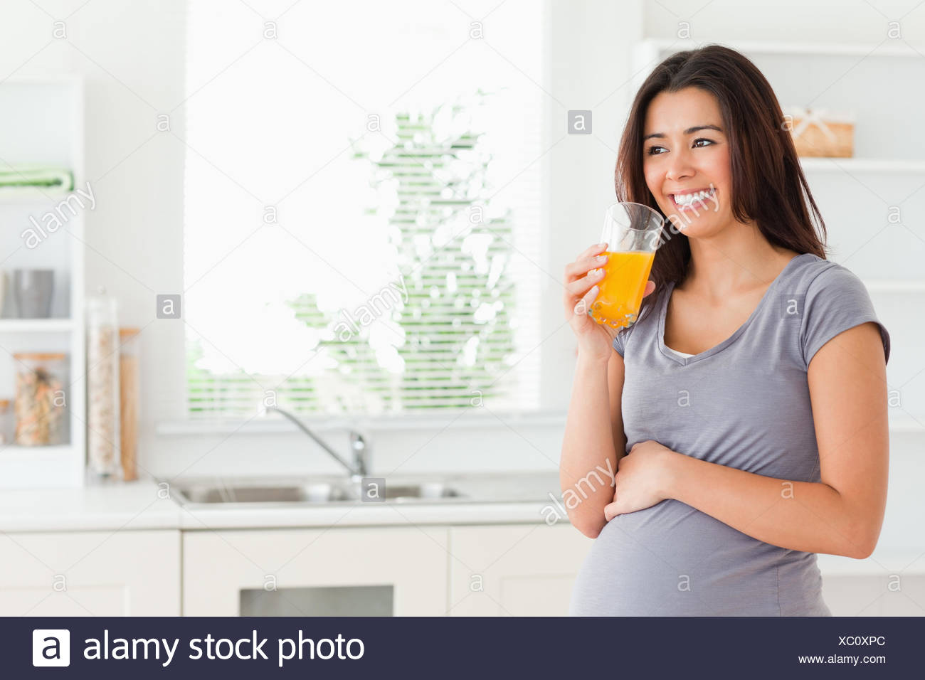 Good looking pregnant woman drinking a glass of orange juice while ...