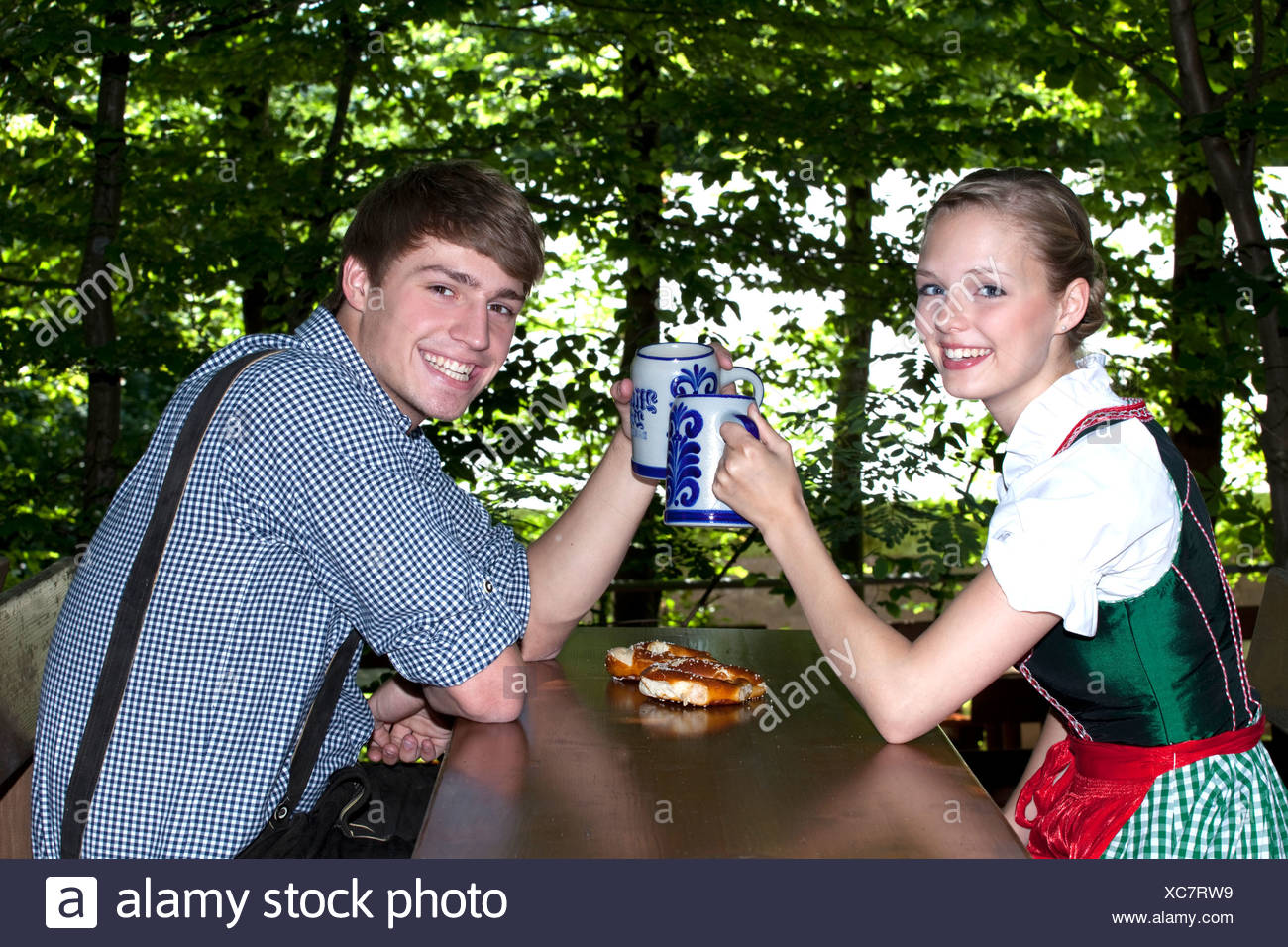 Young Couple In Dirndl And Lederhosen Clinking Their Beer Steins