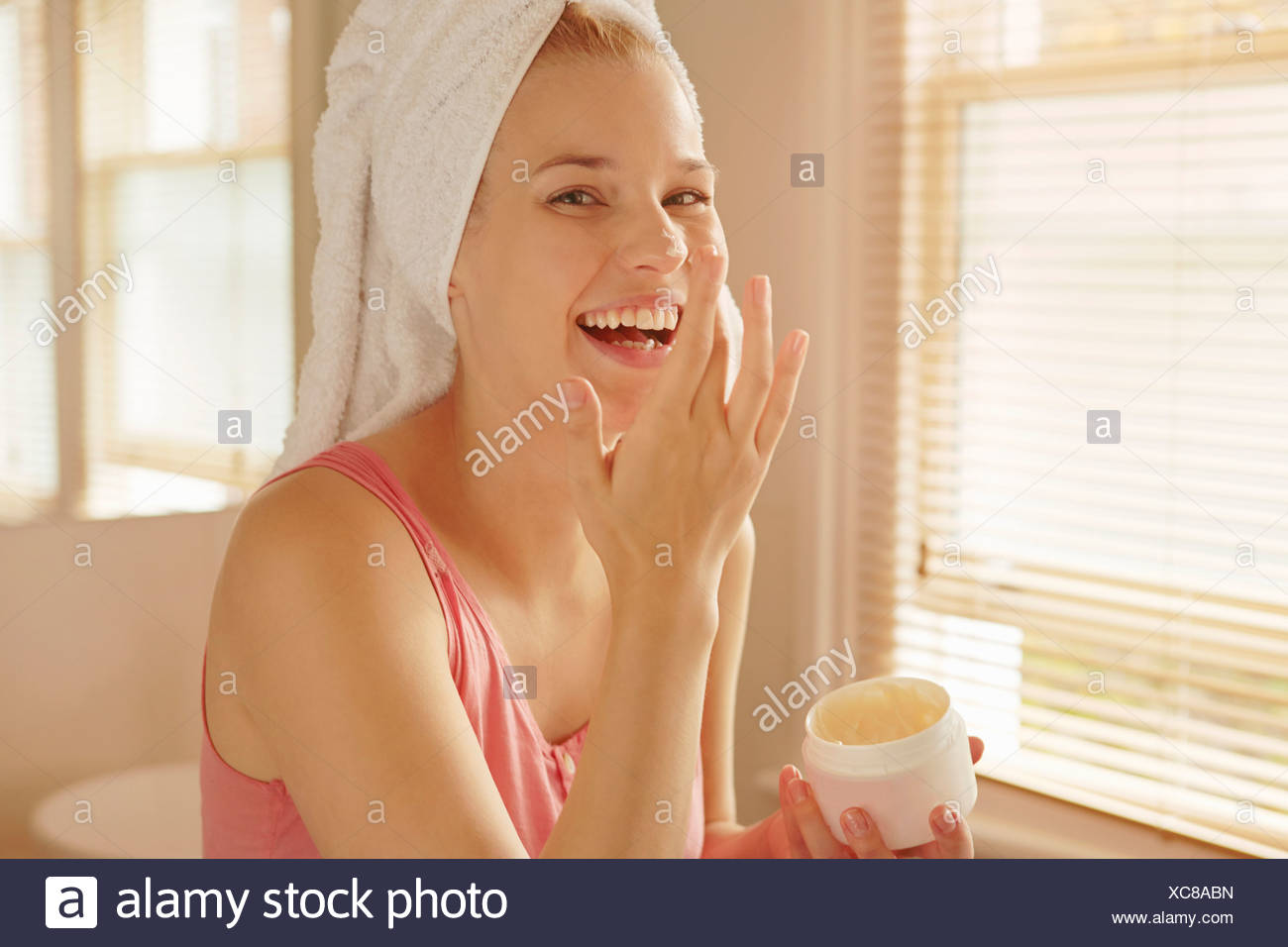 Young woman in bathroom putting on face cream Stock Photo