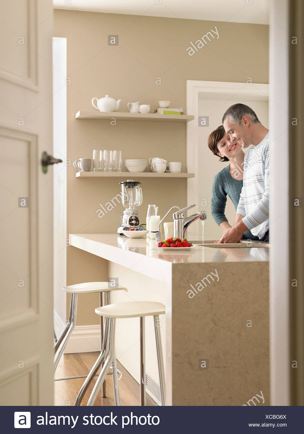 Smiling Couple In Kitchen Seen Through Open Door Stock