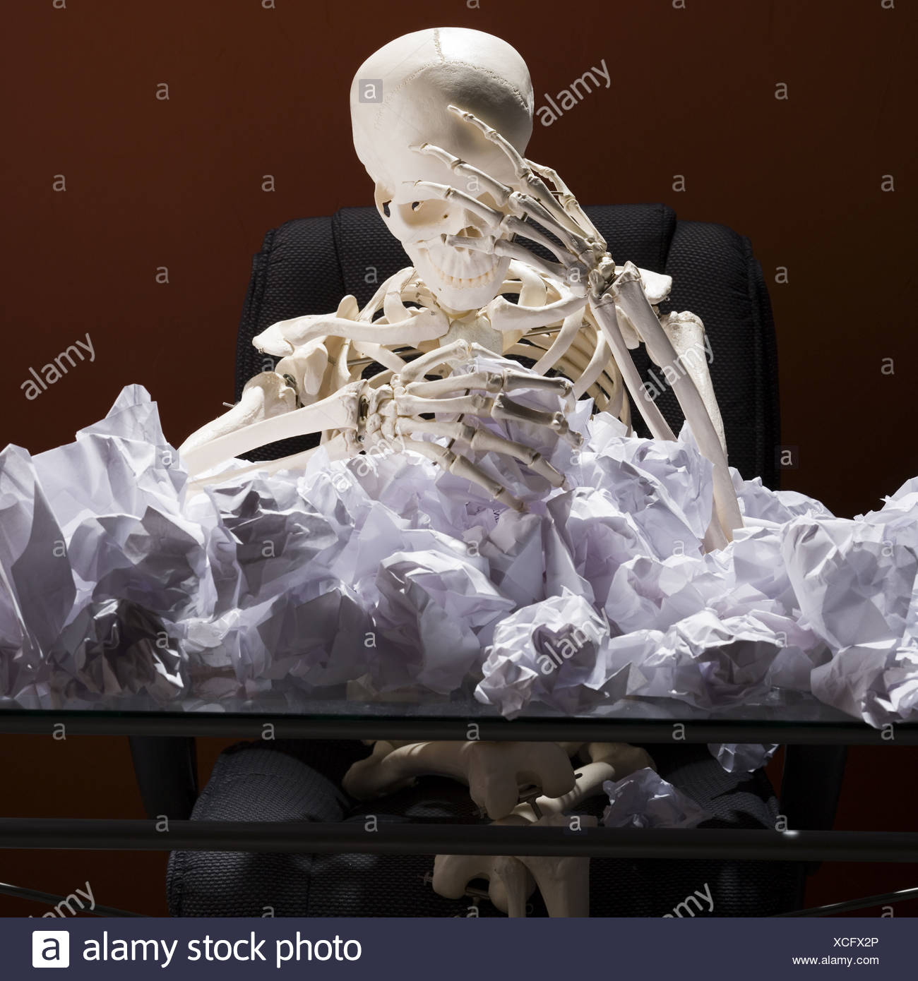 Skeleton Sitting At Desk With Crumpled Papers Stock Photo
