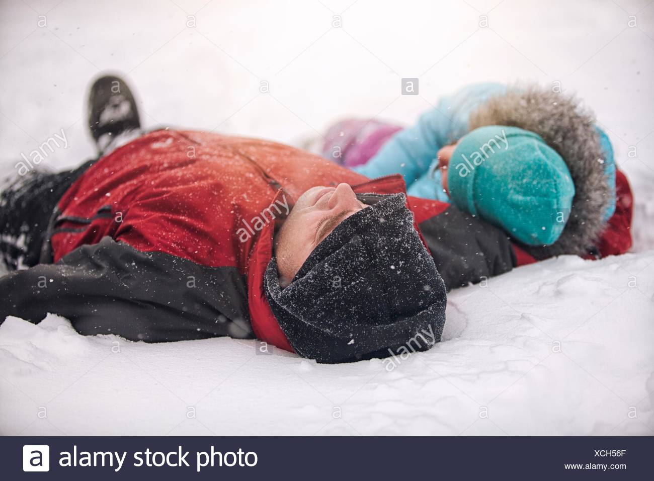 Father and daughter wearing knit hats lying on backs in snow Stock Photo