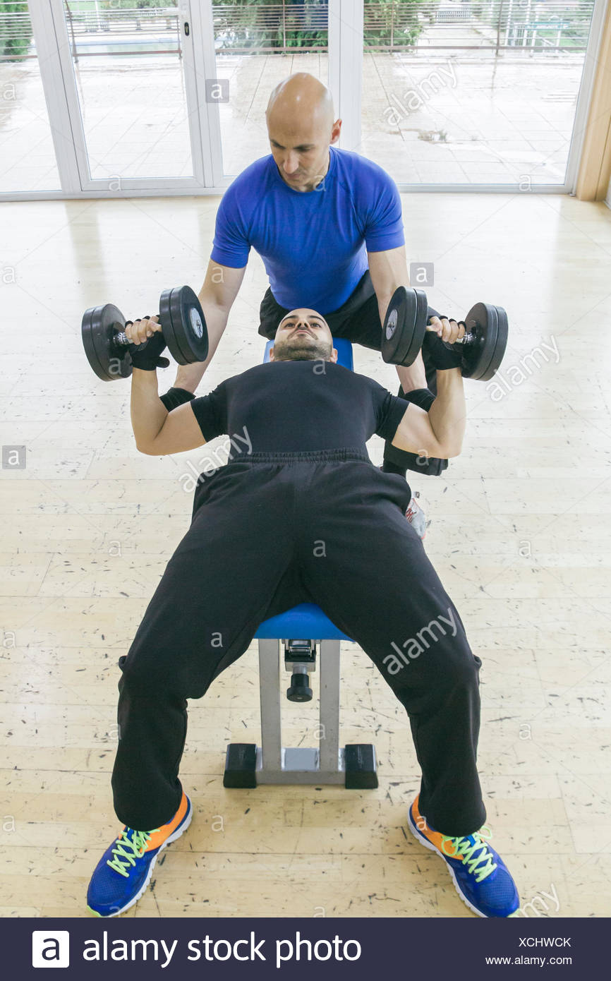 Man Lifting Weights Assisted By A Coach Lying On A Bench Gym Stock