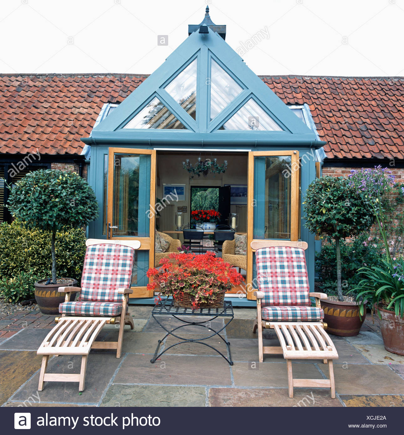 Clipped Trees In Pots Beside Wooden Loungers On Paved Patio Of