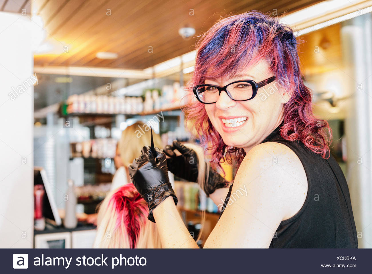 A Hair Colourist In Gloves Applying Red Hair Dye To A Client S