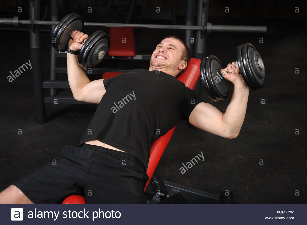 Young Man Doing Dumbbell Incline Bench Press Workout In Gym Stock