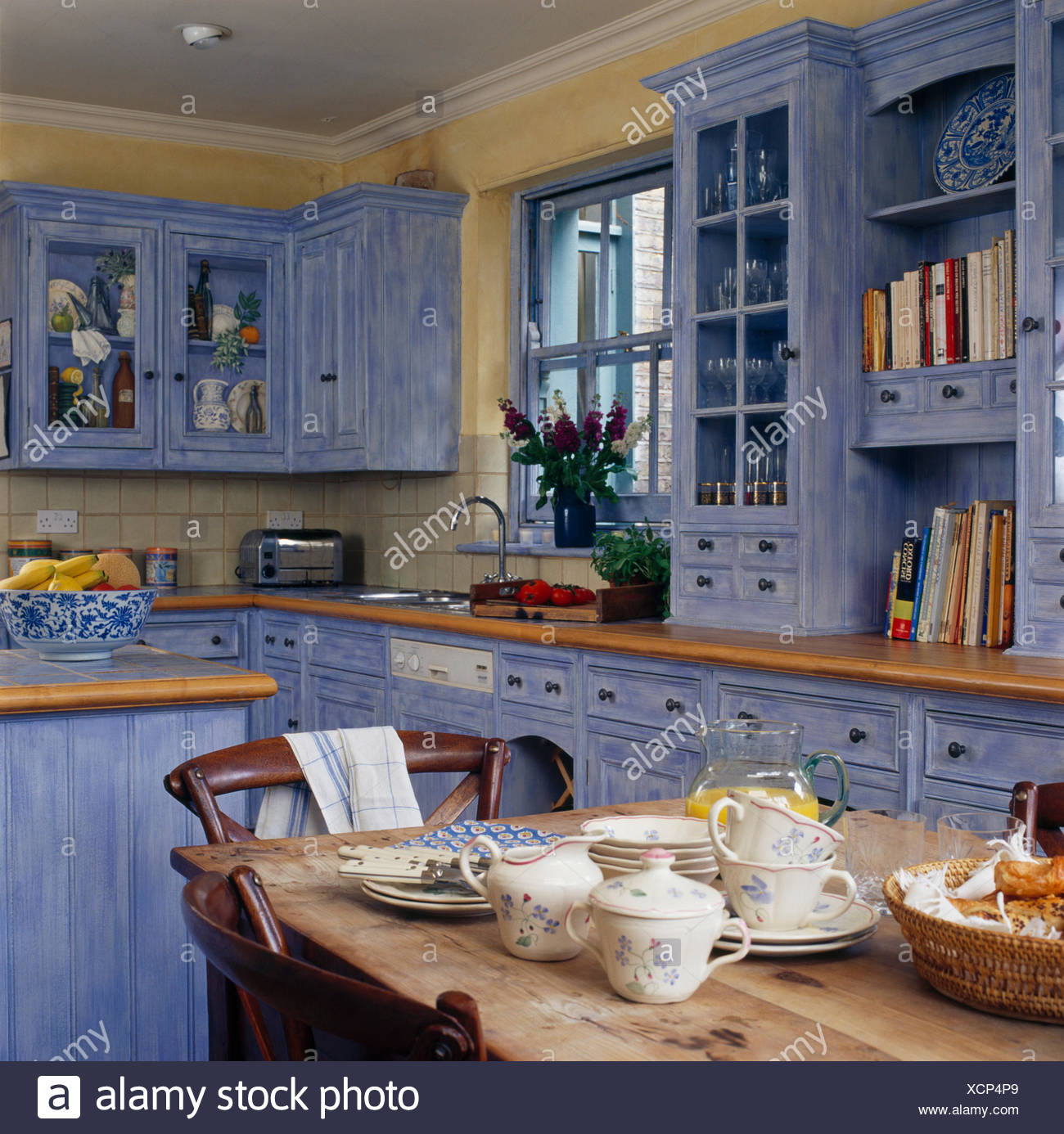Cups And Plates On Pine Table In Country Kitchen With Cupboards