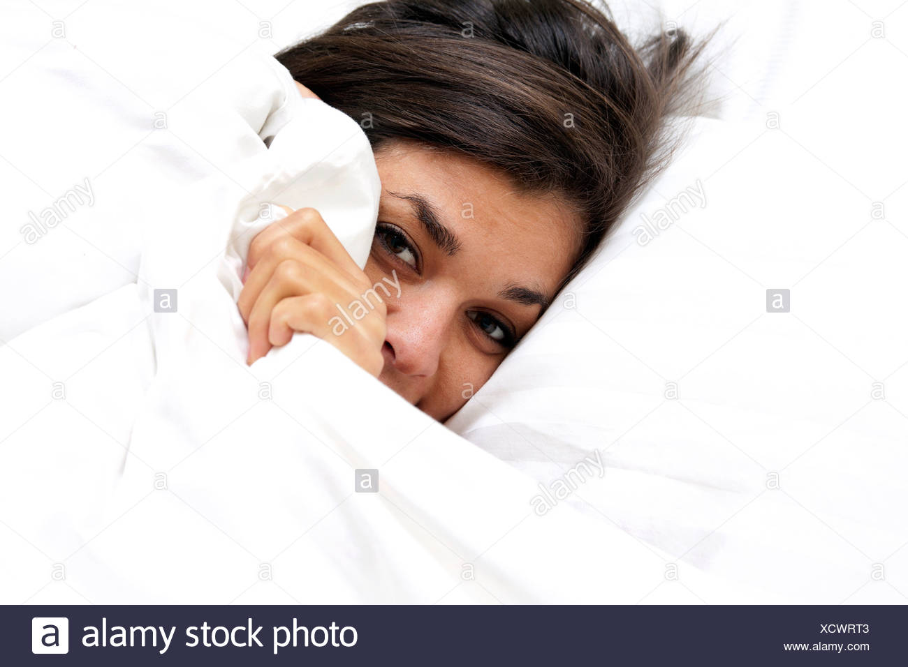 Young Woman Peeping From Under Bed Covers Stock Photo