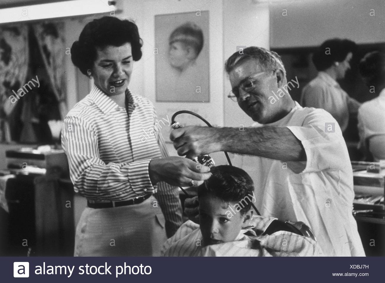 Young Boy Getting His First Haircut From A Barber While His Mother