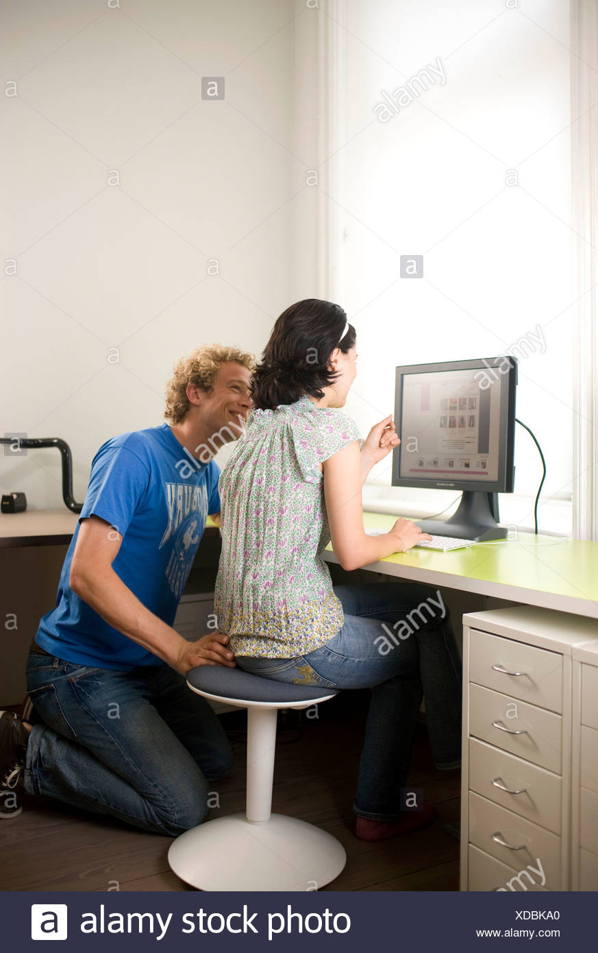 Young Couple Sitting At Desk In Front Of A Computer Stock Photo