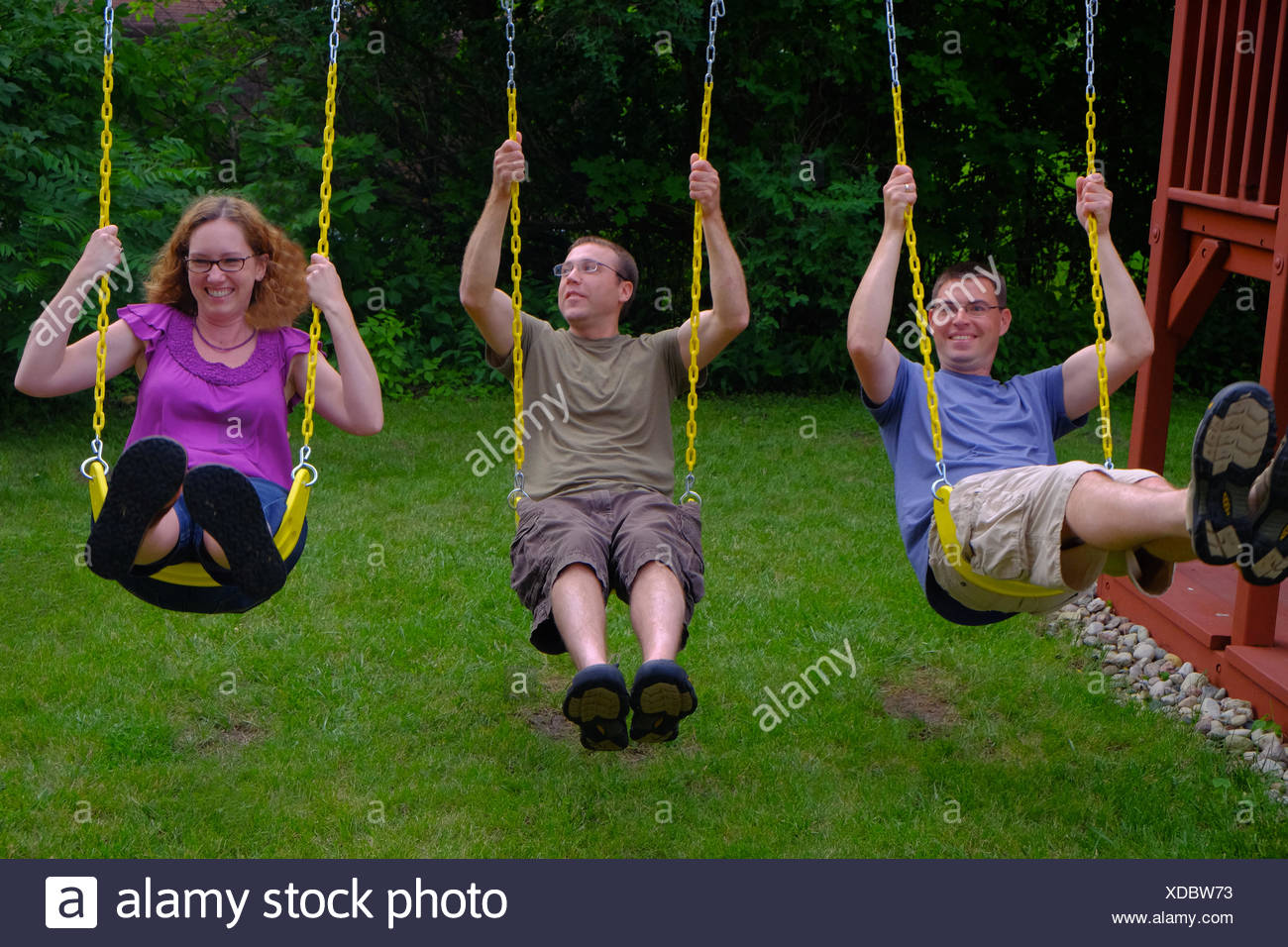 Three Adults Swing On A Swing Set On A Summer Afternoon