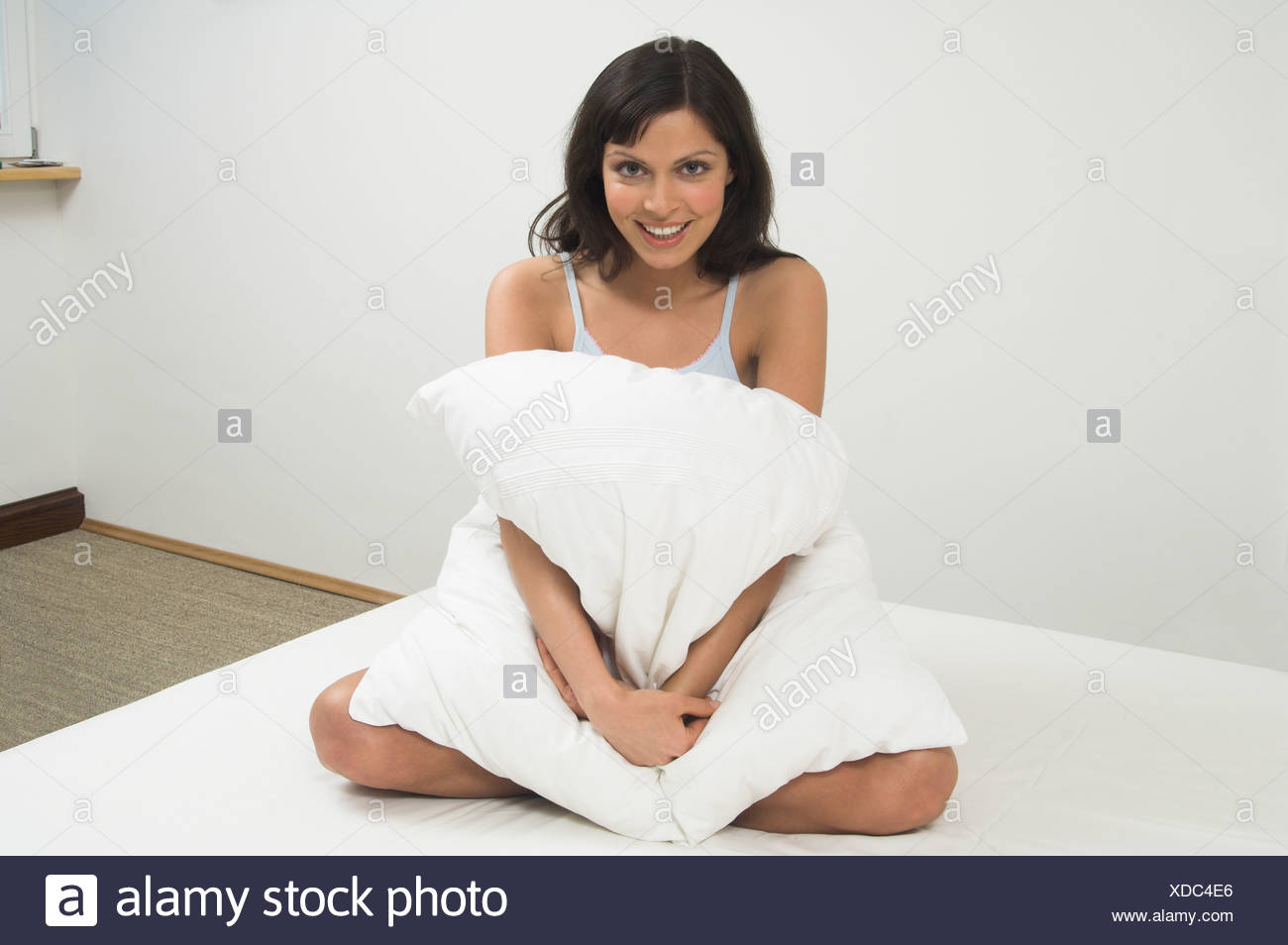 Full Body Portrait Of Young Woman Sitting On Bed And Cuddling