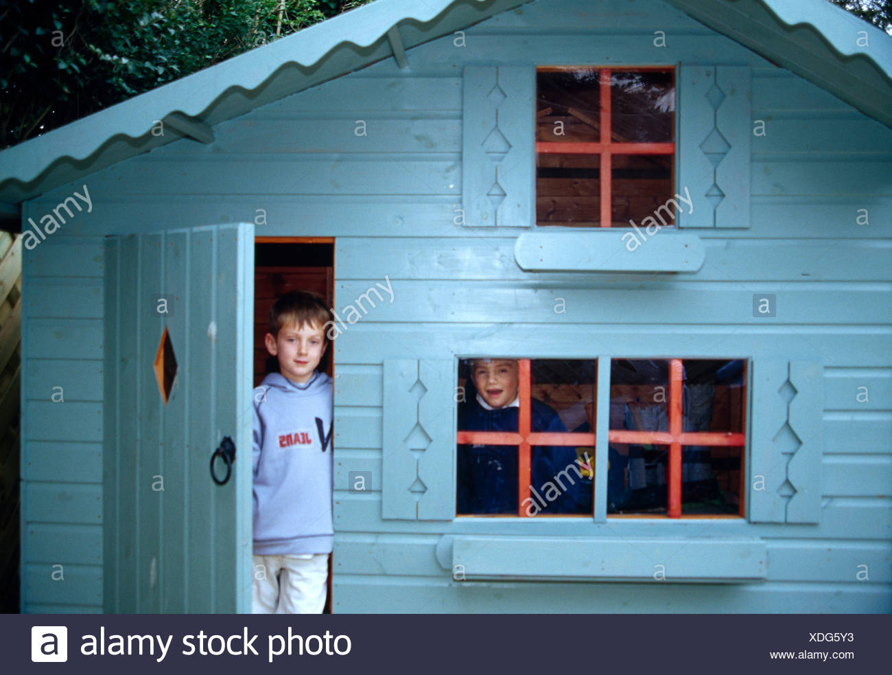 Small Boy Standing In Doorway Of Blue Playhouse With His Brother