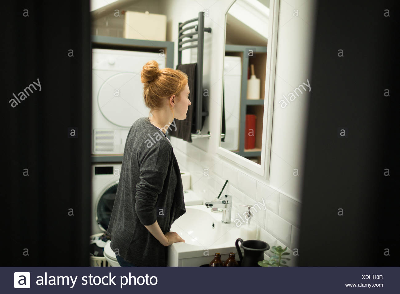 Young woman looking in bathroom mirror Stock Photo