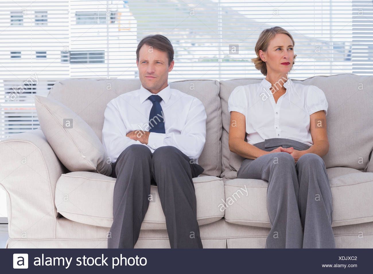 Two Bored Business People Sitting On Couch With Arms Crossed Stock