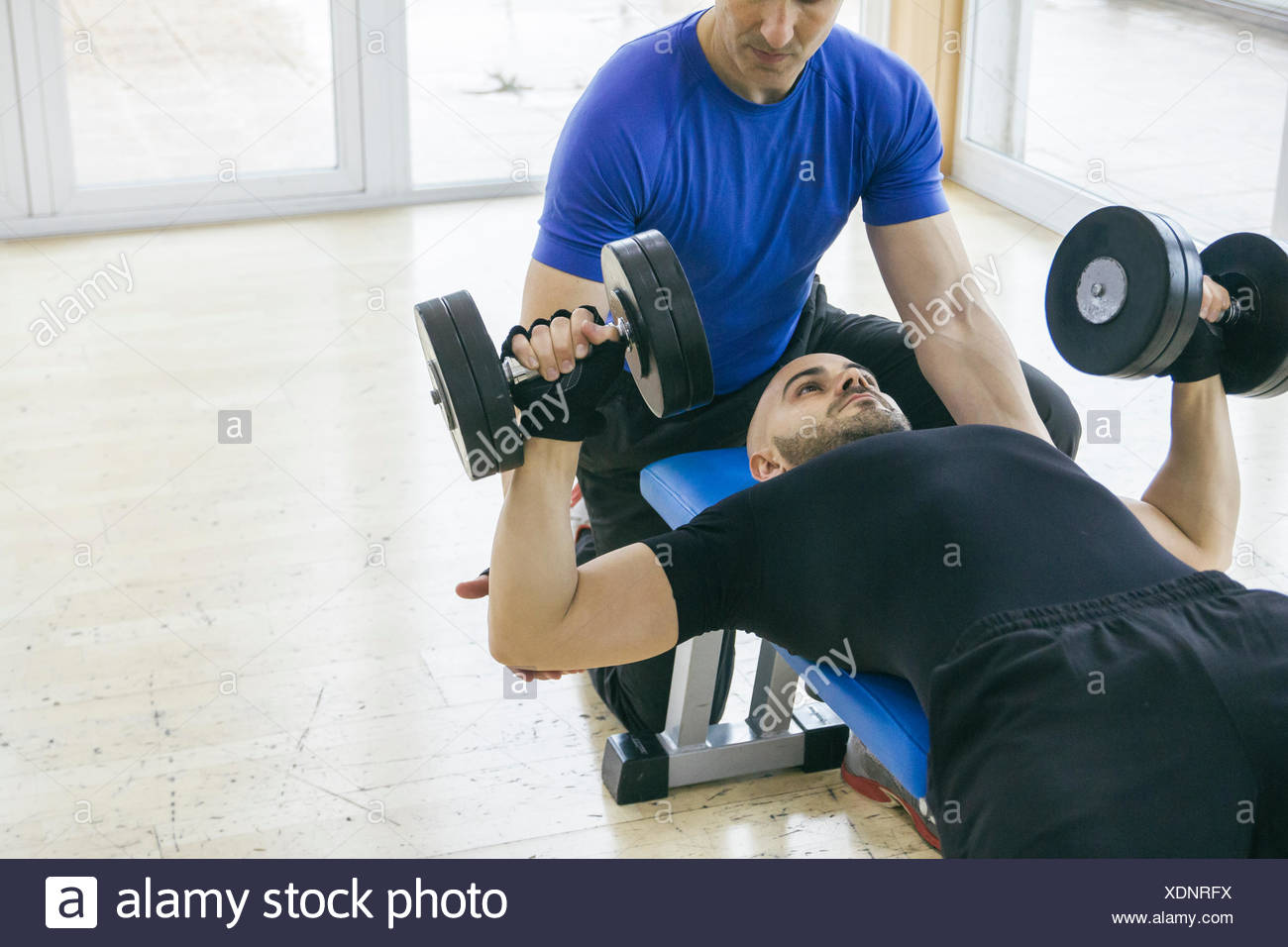 Man Lifting Weights Assisted By A Coach Lying On A Bench Gym Stock