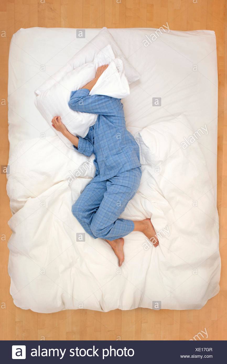 Mid Adult Woman Lying In Bed With Pillow Over Head Stock Photo