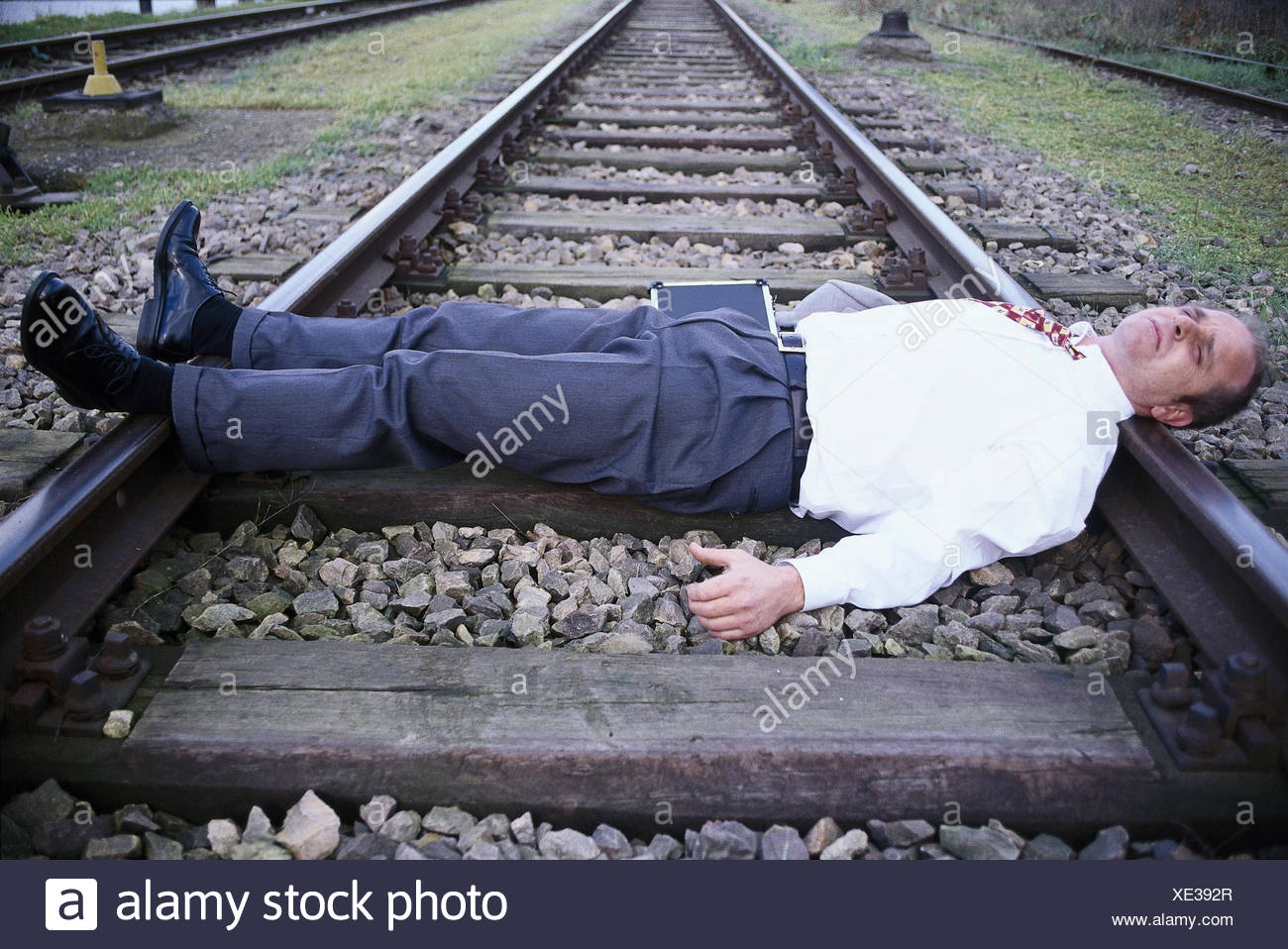 businessman-desperately-lie-tracks-attempted-suicide-business-manager-loss-ruin-failure-bankruptcy-ruins-hopelessness-hopelessness-resignation-facial-play-desperation-discourages-weary-life-suicide-suicide-suicide-attempt-train-tracks-XE392R.jpg