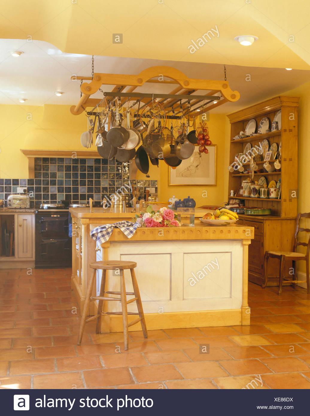 Hanging Pan Rack Above Island Unit In Yellow Kitchen With