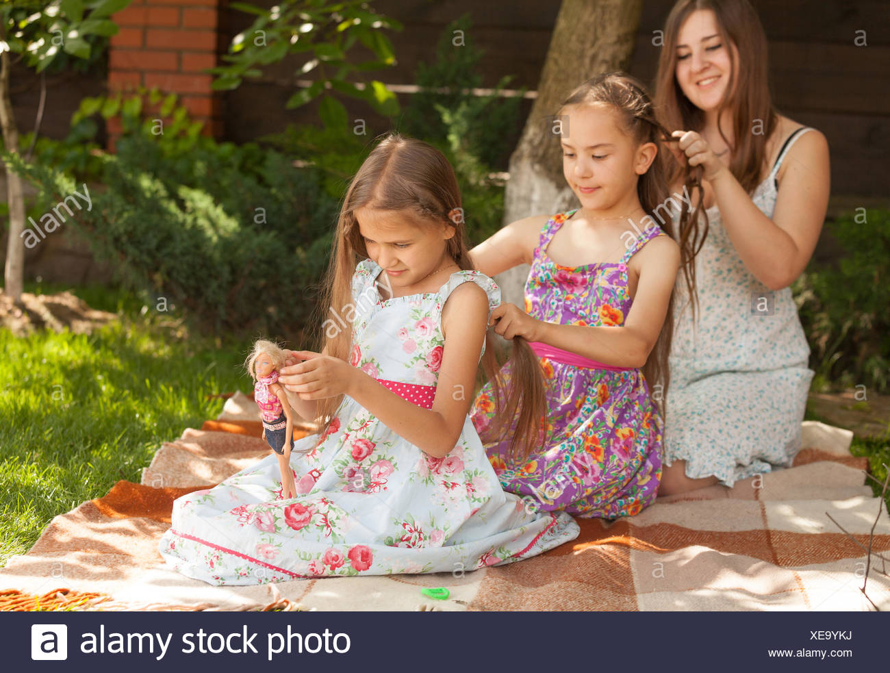 Outdoor Shot Of Mother And Two Daughters Braiding Hair To