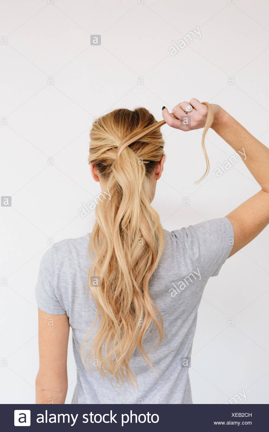 A Young Woman With Long Blond Wavy Hair Tying A Ponytail Back