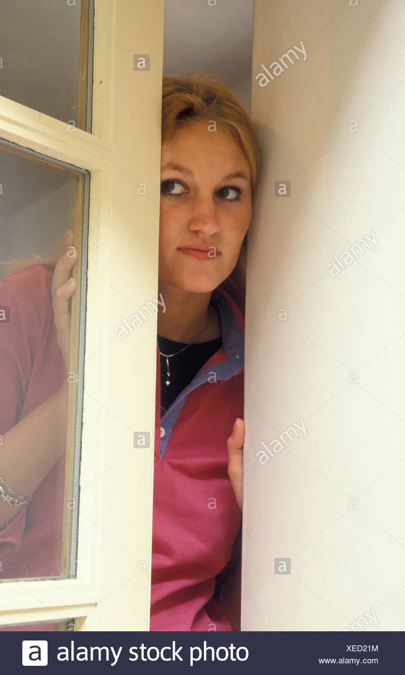 young woman looking suspiciously out of window Stock Photo