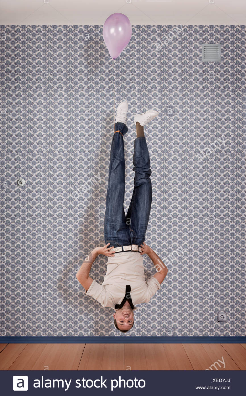 Mature man floating upside down with balloon - Stock Image.