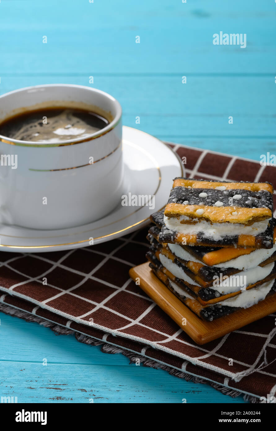 Seitenansicht Tasse Kaffee und Stapel von Sandwich Biscuits mit weißen Cremefüllung vertikalen Zusammensetzung Stockfoto