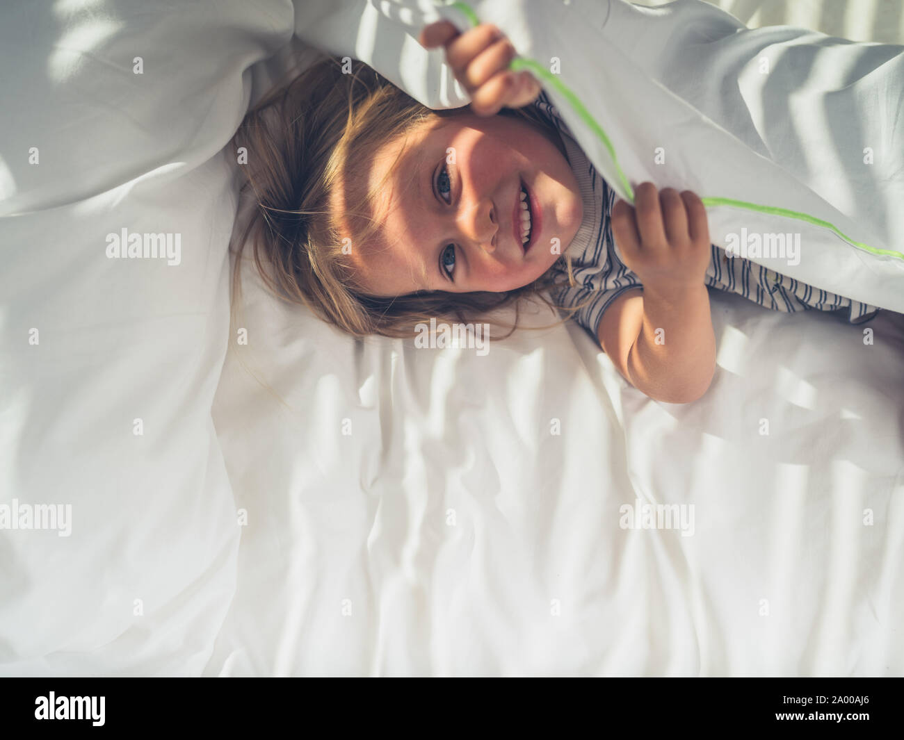 Ein kleines Kind versteckt sich unter den Abdeckungen in einem Bett Stockfoto